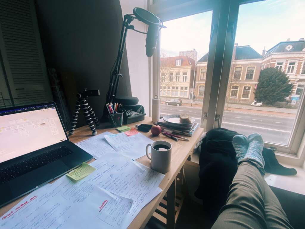 Foto van mijn bureau en het raam, met mijn benen languit in het raamkozijn